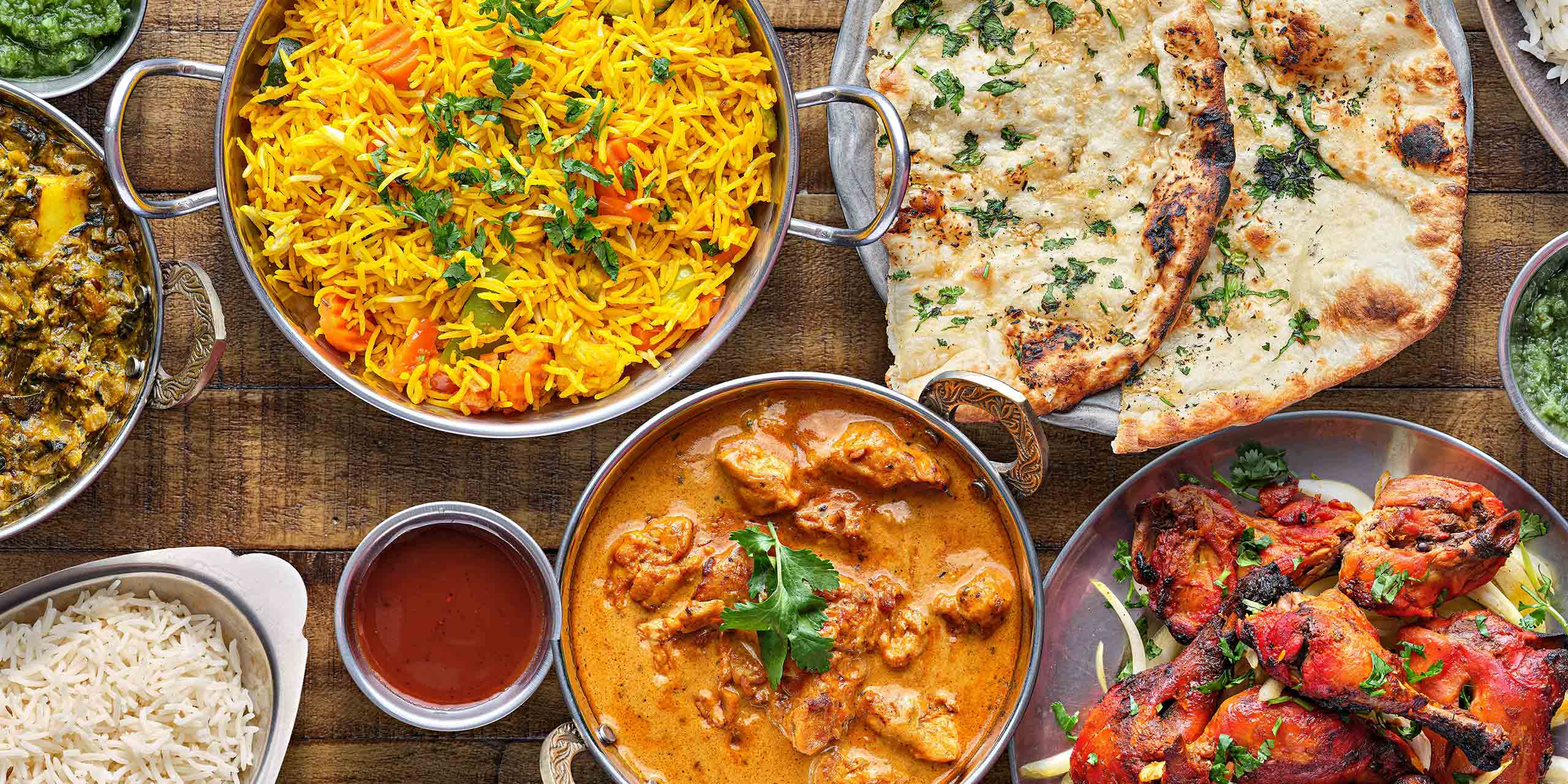 An overhead spread of Punjabi dishes — vegetable pulao, garlic naan, butter chicken and tandoori chicken — on a dark wooden table at Haveli Indian Cuisine in North Conway